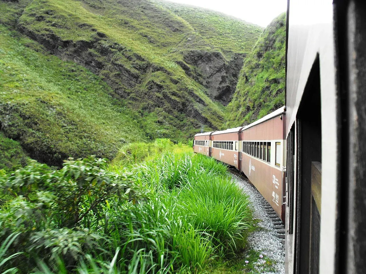 Trem de passageiros atravessando um vale verde na região de Ouro Preto