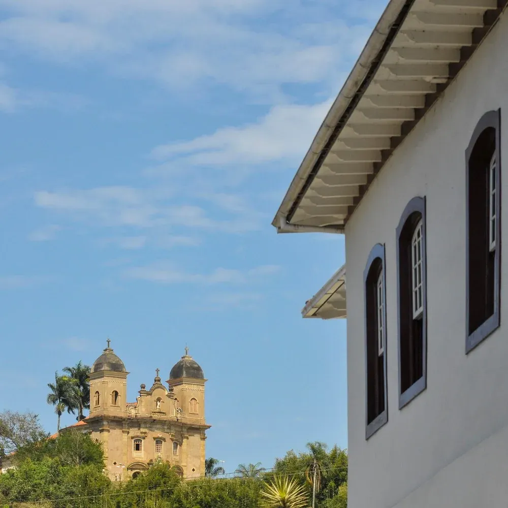 Igreja de São Pedro dos Clérigos entre palmeiras, ao lado de um casarão, em Mariana