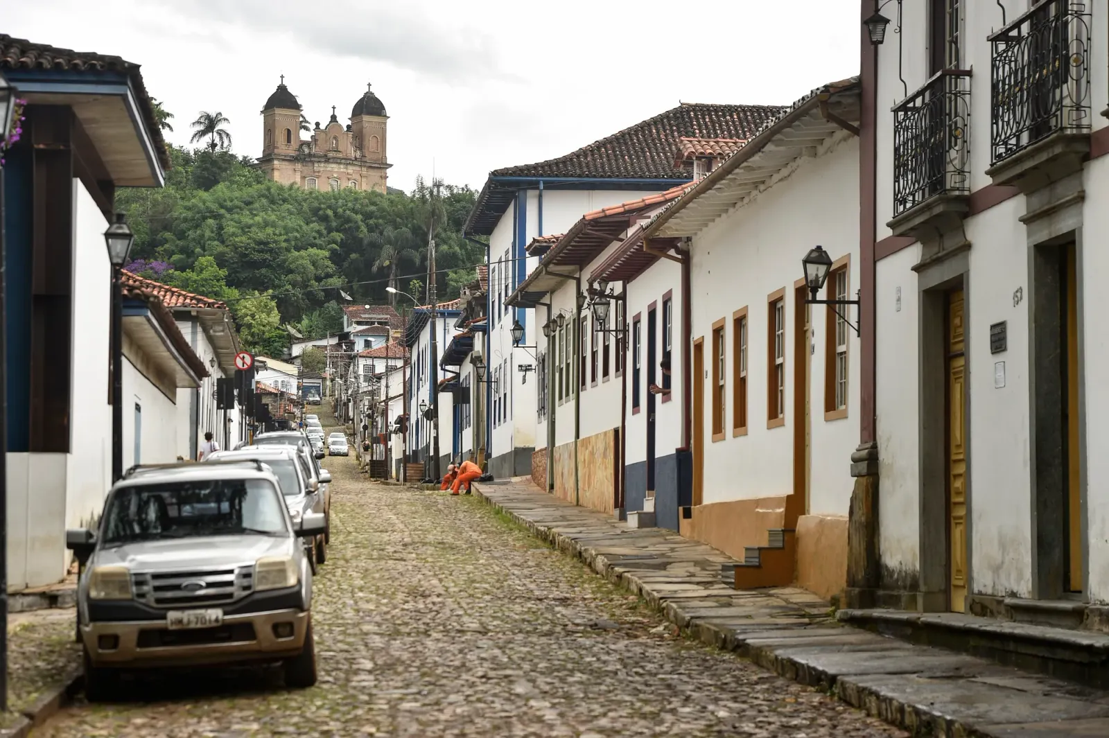 Rua de pedra do centro histórico de Mariana, com casarões e uma igreja no alto da colina