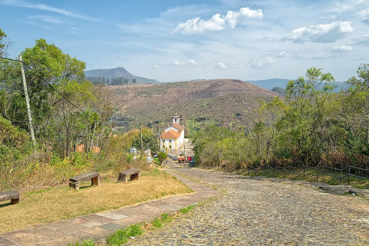 Rua de pedra descendo até uma capela, com morros ao fundo, em Ouro Preto